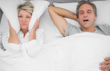 kobieta zakrywa poduszką uszy bo nie może spać z uwagi na chrapanie partnera w łóżku
